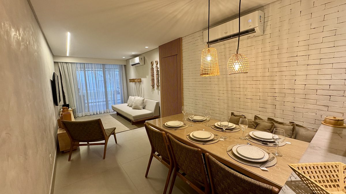 Ambiente integrado com mesa posta para seis, tijolo aparente pintado e pendentes de fibra natural.