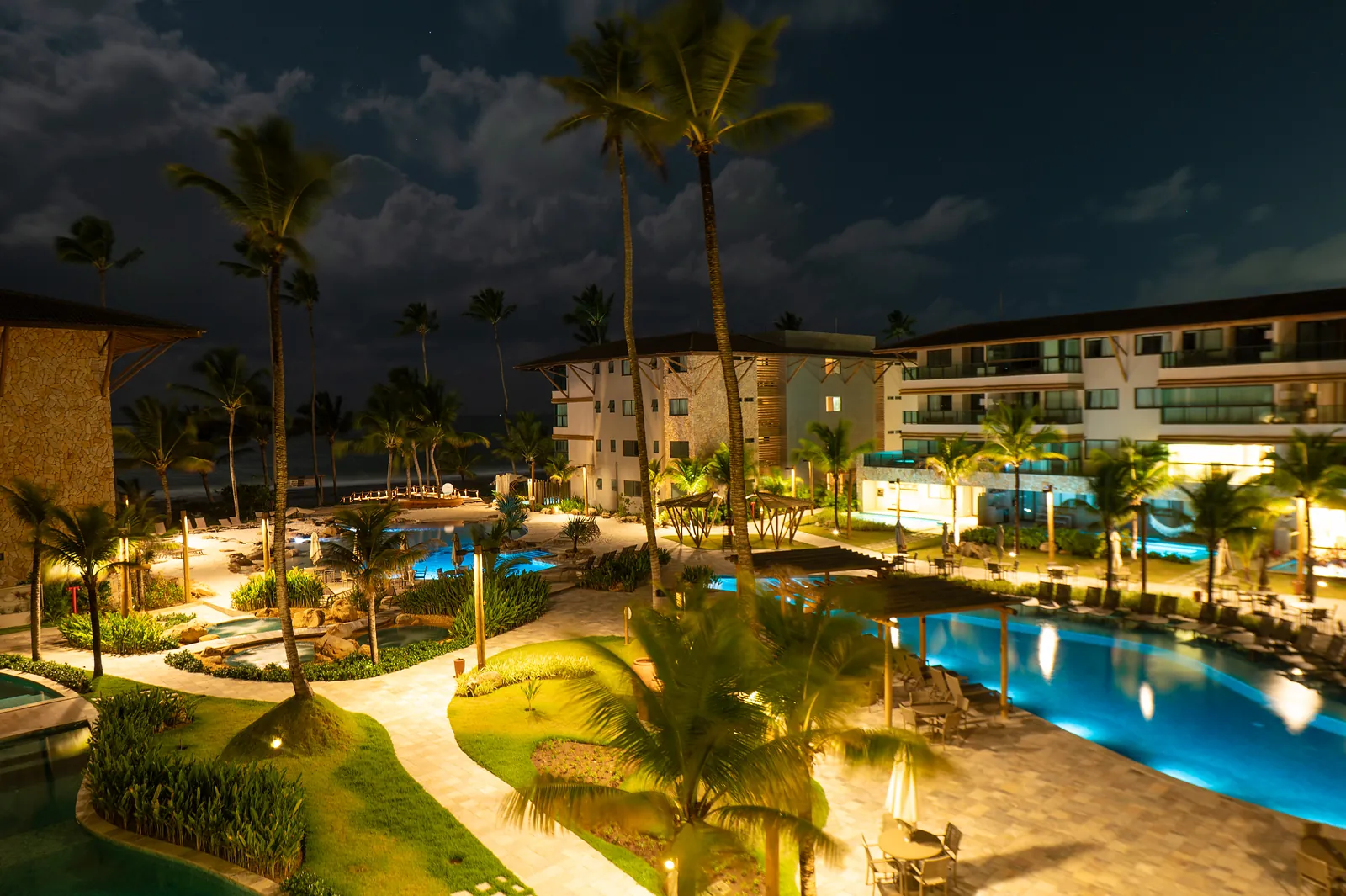 Vista noturna das piscinas iluminadas entre os blocos do resort.