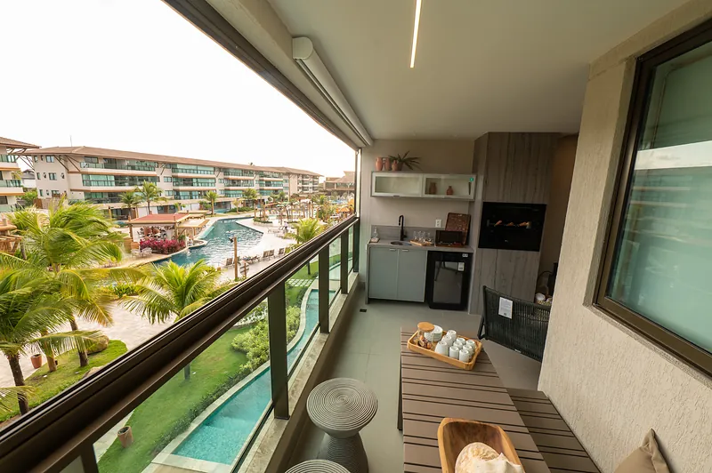 Varanda gourmet de apartamento do Polin\u00e9sia Villa, com churrasqueira, bancada e vista para as piscinas do resort.