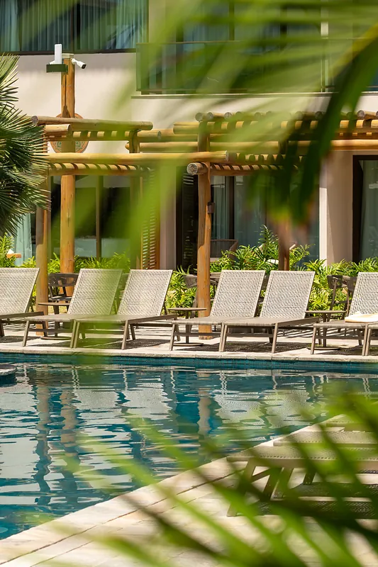 Deck de piscina com espreguiçadeiras à sombra dos coqueiros.