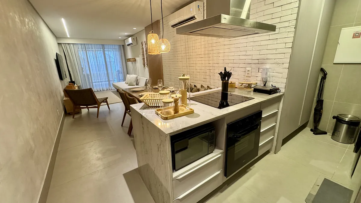 Cozinha com ilha em m\u00e1rmore, forno e cooktop embutidos, aberta para a sala.